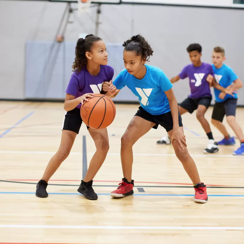 Two girls play basketball in a gym.
