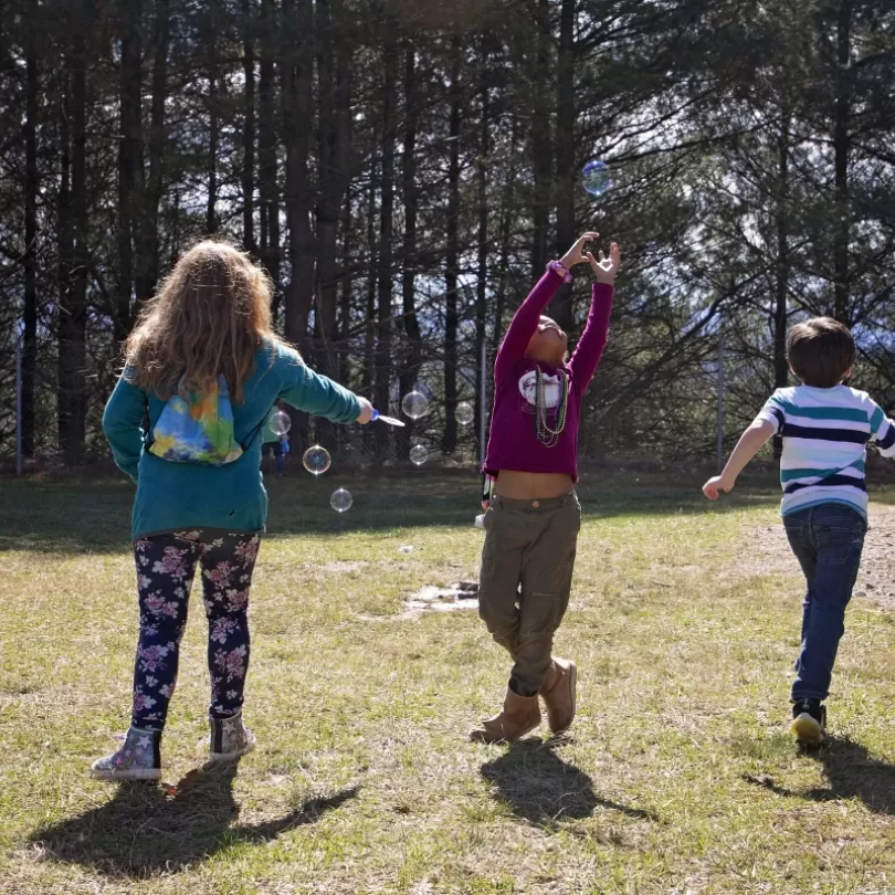 Three kids playing with bubbles outside 
