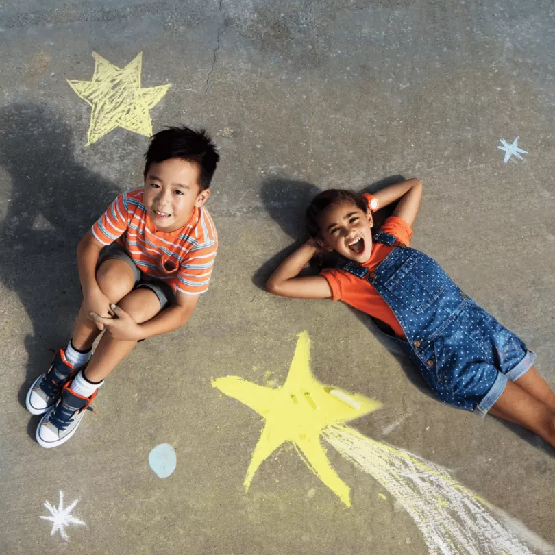 Two kids play with chalk outside.
