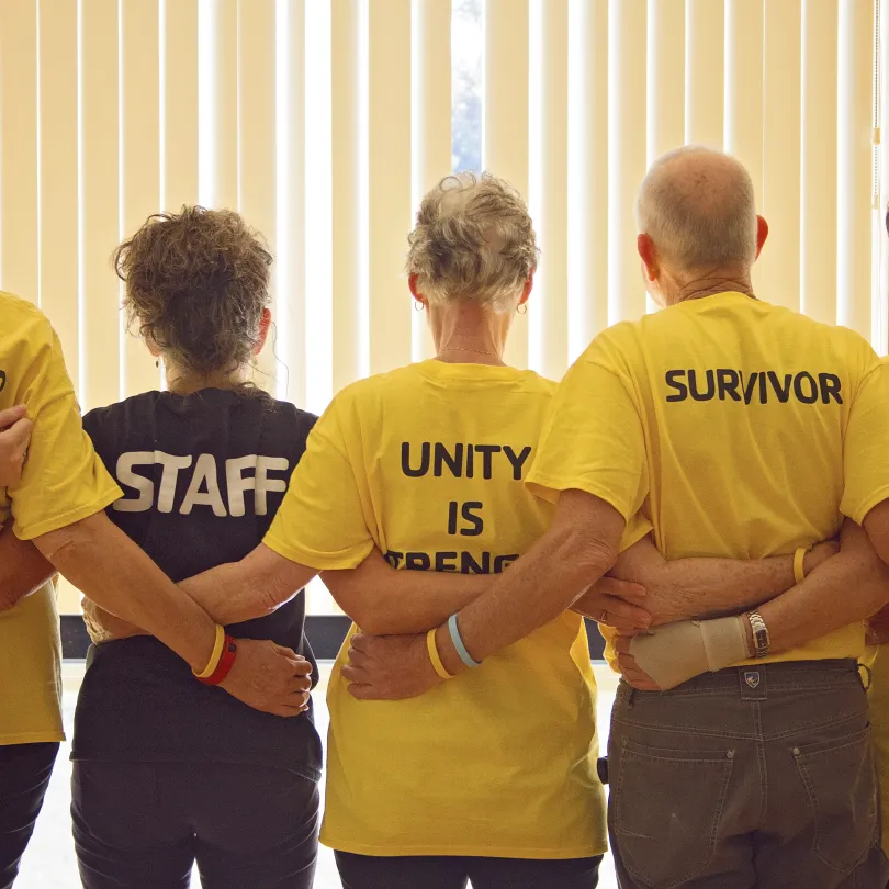 A group of people stand together with their arms around each other during a Livestrong program.